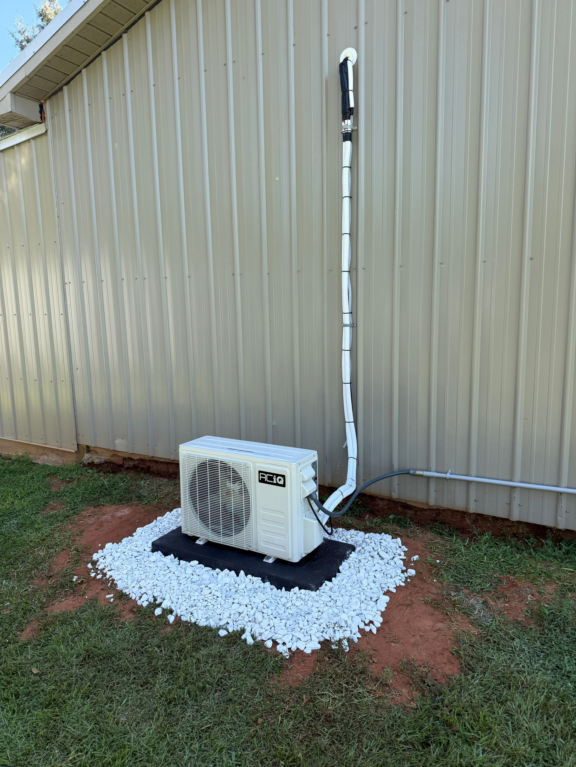 ACIQ mini-split outdoor unit secured to a new pad beside a metal exterior wall in Loxley